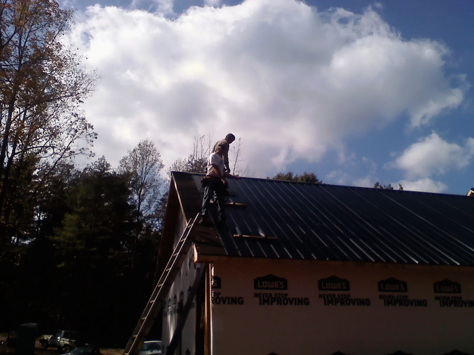 Roofer fastening dark metal panels high against a cloudy sky, from a Roof Inspection job in Manville