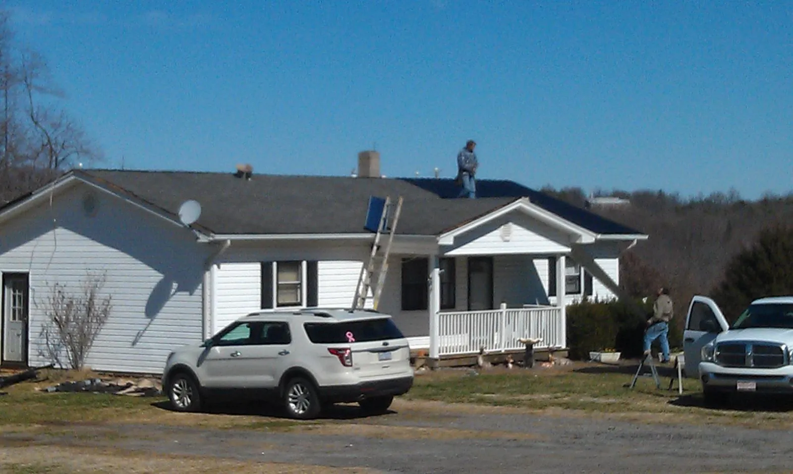 Roofers stripping shingles from a white ranch house roof in Manville