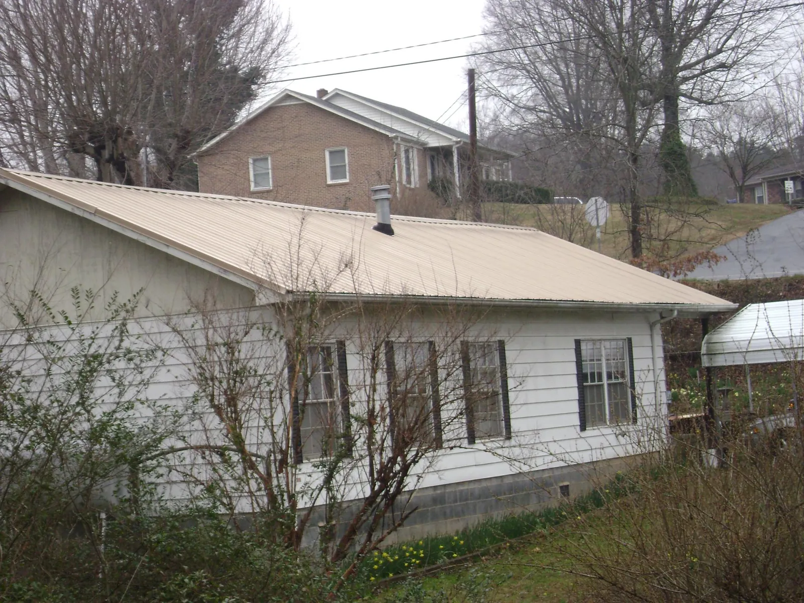 Tan metal roof on a white sided house set into a hillside — Commercial Roofing by Roofing Brothers in Manville